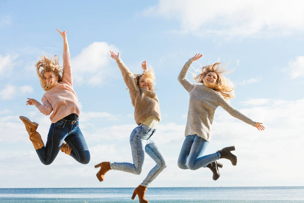 Three women full of joy jumping around with sky in background. Female friends having fun outdoor. - Фото, изображение