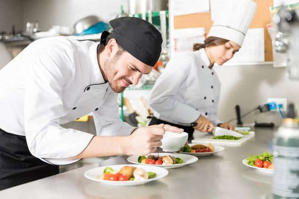 усміхнений професійний кухар наливає соус на смачну страву на кухні
 - Фото, зображення