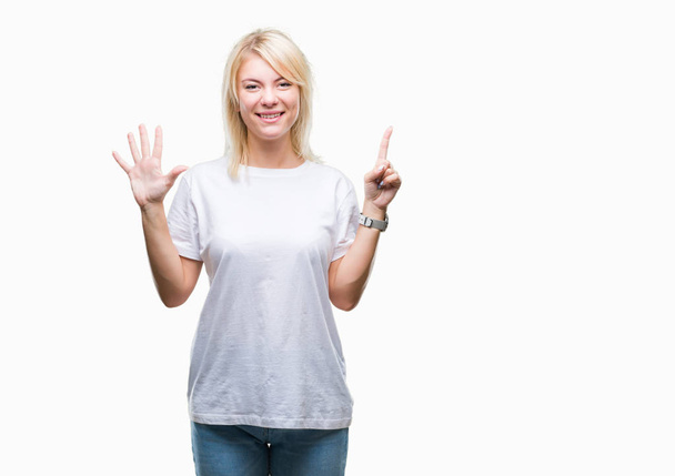 Νέοι όμορφη ξανθιά γυναίκα, φορώντας άσπρο t-shirt πάνω από το απομονωμένο φόντο δείχνει και δείχνει προς τα επάνω με τα δάχτυλα αριθμός έξι ενώ χαμογελώντας αυτοπεποίθηση και χαρούμενοι. - Φωτογραφία, εικόνα