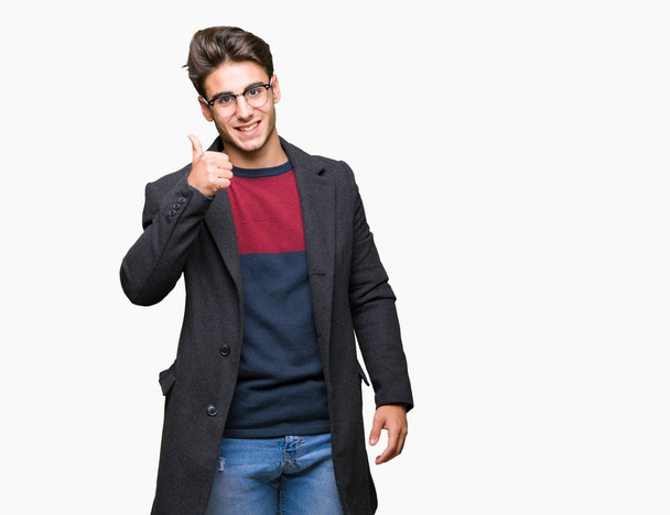 Mladý pohledný elegantní muž nosí brýle izolované pozadí dělá šťastné palec nahoru gesto rukou. Schvalování výraz s ukazuje úspěch při pohledu na fotoaparát. - Fotografie, Obrázek