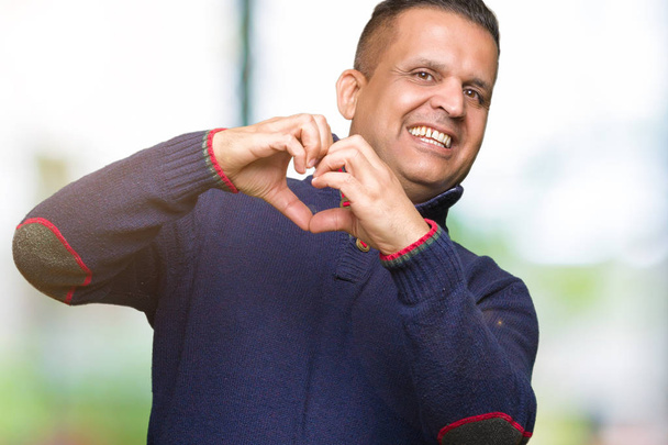 Hombre árabe de mediana edad sobre un fondo aislado sonriendo en el amor mostrando el símbolo del corazón y la forma con las manos. Concepto romántico
. - Foto, imagen