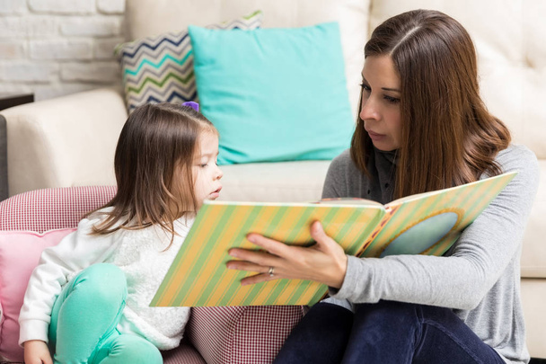 Erwachsene Frau liest Geschichte für neugierige Tochter zu Hause - Foto, Bild