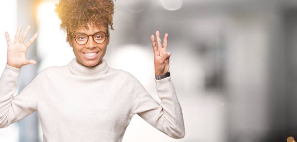 Mooie jonge african american vrouw dragen bril over geïsoleerde achtergrond weergeven en met de vingers omhoog nummer acht terwijl lacht zelfverzekerd en blij. - Foto, afbeelding