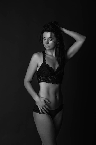 Sexy body of young attractive woman. Beautiful sporty lady in black bikini against dark background. Black and white photography - Foto, imagen