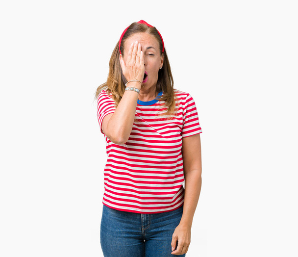schöne Frau mittleren Alters in lässigen Streifen T-Shirt über isoliertem Hintergrund gähnen müde bedeckt das halbe Gesicht, Augen und Mund mit der Hand. Gesicht schmerzt vor Schmerzen. - Foto, Bild