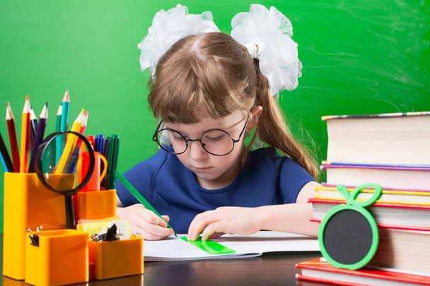 Enfant femelle dans des lunettes et des arcs blancs faisant la ligne avec crayon vert sur papier vue de côté
 - Photo, image