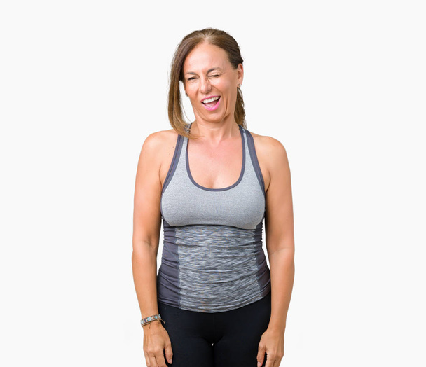 Beautiful middle age woman wearing sport clothes over isolated background winking looking at the camera with sexy expression, cheerful and happy face. - Fotó, kép