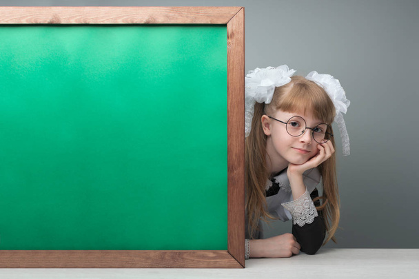Smiling female kid with tails and glasses presenting green chalkboard with copy space - Fotó, kép