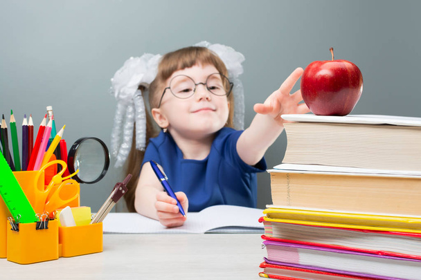 Jolie fille en uniforme scolaire assis à la table et s'étire pour une pomme rouge
 - Photo, image