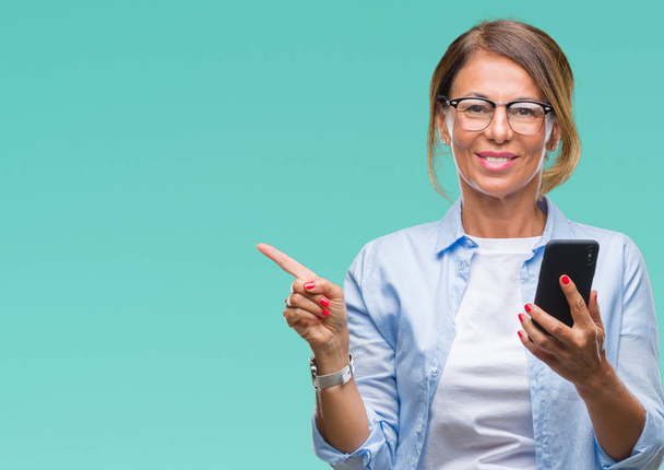 Middle age senior woman texting sending message using smartphone over isolated background very happy pointing with hand and finger to the side - Photo, Image
