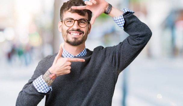 Young handsome smart man wearing glasses over isolated background smiling making frame with hands and fingers with happy face. Creativity and photography concept. - Zdjęcie, obraz