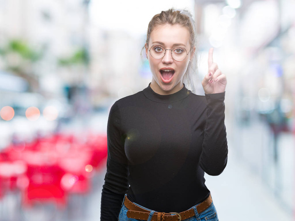 Young blonde woman wearing glasses over isolated background pointing finger up with successful idea. Exited and happy. Number one. - Photo, Image