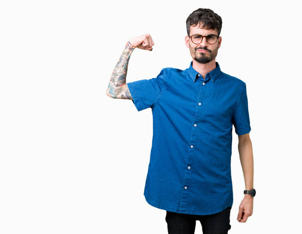 Jovem homem bonito usando óculos sobre fundo isolado Pessoa forte mostrando músculo do braço, confiante e orgulhoso do poder
 - Foto, Imagem