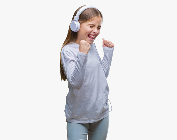 Menina bonita jovem usando fones de ouvido ouvir música sobre fundo isolado muito feliz e animado fazendo gesto vencedor com os braços levantados, sorrindo e gritando para o sucesso. Conceito de celebração
. - Foto, Imagem