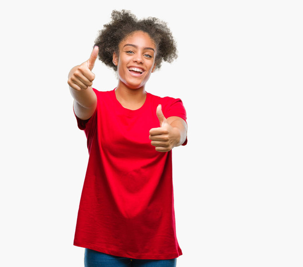 Jovem afro-americana sobre fundo isolado aprovando fazer gesto positivo com a mão, polegares para cima sorrindo e feliz pelo sucesso. Olhando para a câmera, gesto vencedor
. - Foto, Imagem