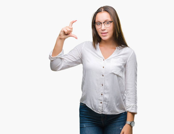 Young caucasian beautiful business woman wearing glasses over isolated background smiling and confident gesturing with hand doing size sign with fingers while looking and the camera. Measure concept. - Photo, Image