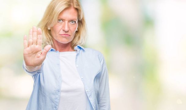 Middle age blonde woman over isolated background doing stop sing with palm of the hand. Warning expression with negative and serious gesture on the face. - 写真・画像