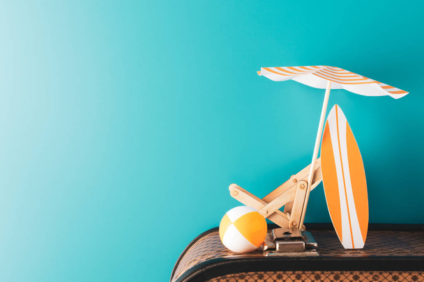 Paraguas de verano con tabla de surf naranja chaise-longue de madera y bola inflable en el equipaje sobre fondo azul
 - Foto, imagen