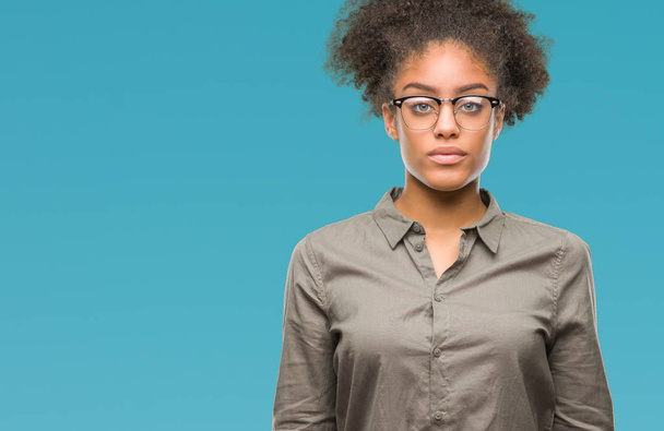 Young afro american woman wearing glasses over isolated background with serious expression on face. Simple and natural looking at the camera. - Foto, Imagen