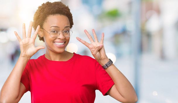 孤立した背景表示と指で上向きに眼鏡をかけて美しい若いアフリカ系アメリカ人女性ナンバー ナイン自信を持って、幸せな笑みを浮かべて、. - 写真・画像