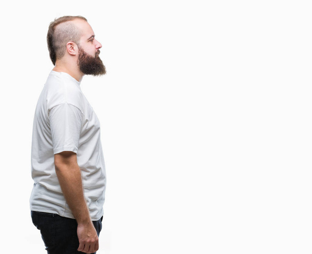 junger kaukasischer Hipster mit lässigem T-Shirt über isoliertem Hintergrund, der zur Seite schaut, entspannter Profilpose mit natürlichem Gesicht und selbstbewusstem Lächeln. - Foto, Bild