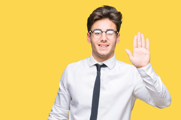 Молодой бизнесмен в очках на изолированном фоне отказывается говорить привет счастливый и улыбающийся, дружественный жест приветствия
 - Фото, изображение