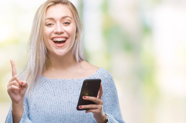若いブロンドの女性のテキスト メッセージ送信メッセージをスマート フォンを使用して分離されたアイデアや質問、ナンバーワンの幸せそうな顔で指を指していると驚かれる背景 - 写真・画像