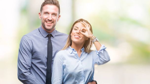 Молодые рабочие деловая пара на изолированном фоне делает хорошо жест с улыбкой рукой, глаза смотрят сквозь пальцы с счастливым лицом
. - Фото, изображение