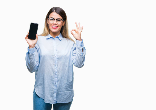 Молода красива ділова жінка, що показує порожній екран смартфона на ізольованому фоні, робить знак з пальцями, відмінний символ
 - Фото, зображення