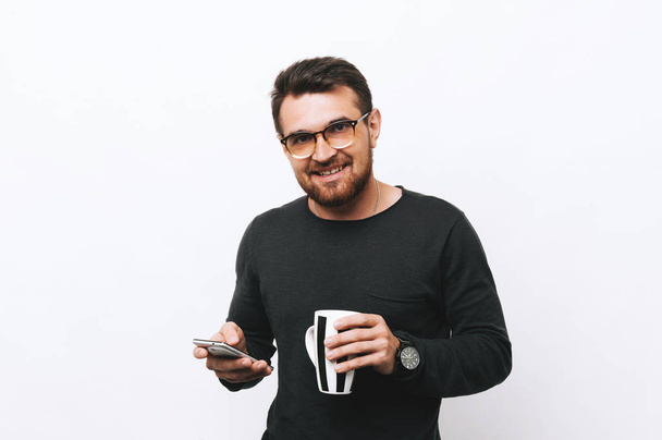 Happy man holds in hand cup with coffee and usiing mobile - Photo, Image