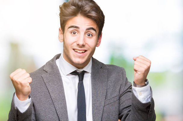 Young business man wearing suit and tie over isolated background celebrating surprised and amazed for success with arms raised and open eyes. Winner concept. - Фото, изображение