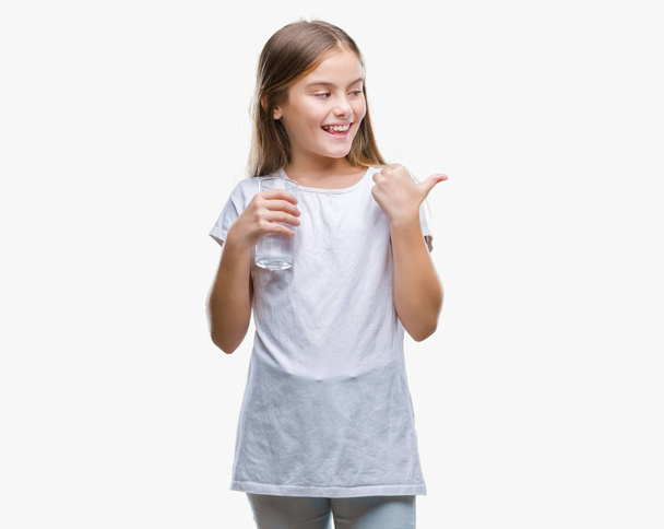 Genç güzel kız işaret ve başparmak kadar mutlu yüz gülümseyen tarafı ile gösteren izole arka plan üzerinde bardak su içme - Fotoğraf, Görsel