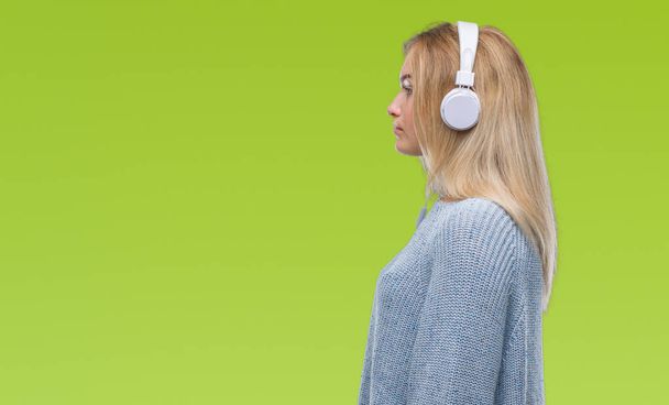 Nuori valkoihoinen nainen kuuntelee musiikkia yllään kuulokkeet yli eristetty tausta etsii sivulle, rentoutua profiili aiheuttaa luonnolliset kasvot luottavainen hymy
. - Valokuva, kuva