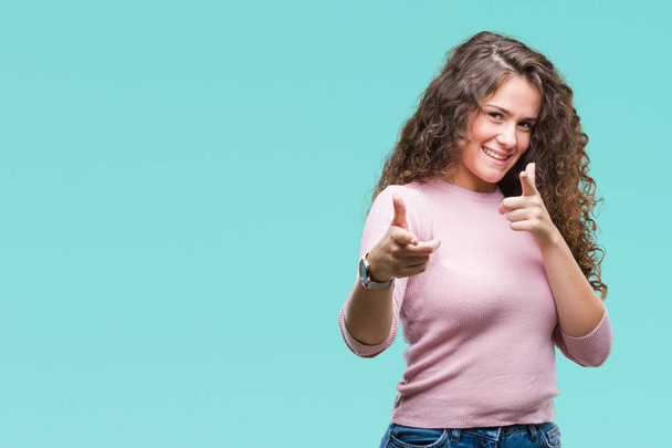 Beautiful brunette curly hair young girl wearing pink sweater over isolated background pointing fingers to camera with happy and funny face. Good energy and vibes. - Photo, Image