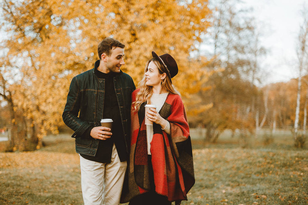 Young cheerful couple walking in autumn park with coffee cuos - Photo, Image