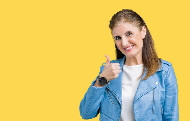 Beautiful middle age mature woman wearing fashion leather jacket over isolated background doing happy thumbs up gesture with hand. Approving expression looking at the camera showing success. - Photo, Image