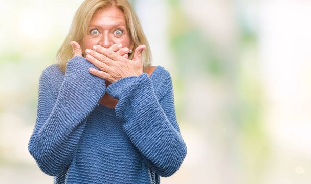 Mujer rubia de mediana edad con suéter de invierno sobre fondo aislado impactó cubriendo la boca con las manos por error. Concepto secreto
. - Foto, imagen