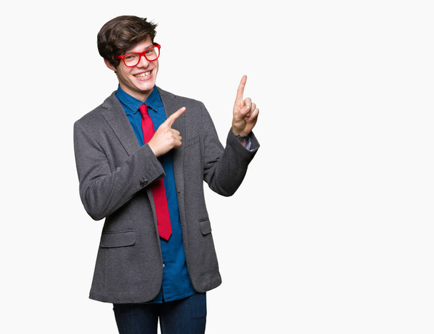 Młody przystojny biznesmen w okularach czerwony na białym tle uśmiechając się i patrząc na kamery, wskazując z dwóch rąk i palców na bok. - Zdjęcie, obraz