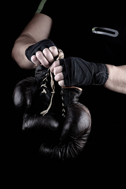  par de guantes deportivos de boxeo muy viejos en las manos de los hombres rebobinado con un vendaje negro
 - Foto, Imagen