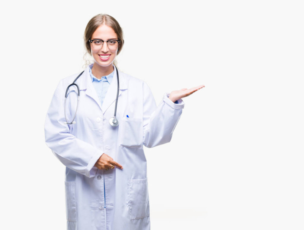 Piękna Młoda Blondynka lekarz kobieta noszenia uniform medyczny na białym tle tło uśmiechający się wesoły prezentacji i wskazując z dłonią, patrząc na kamery. - Zdjęcie, obraz