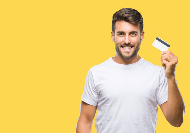 Young handsome man holding credit card over isolated background with a happy face standing and smiling with a confident smile showing teeth - Fotó, kép
