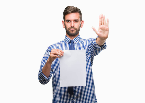 Young handsome man holding blank paper over isolated background with open hand doing stop sign with serious and confident expression, defense gesture - Φωτογραφία, εικόνα