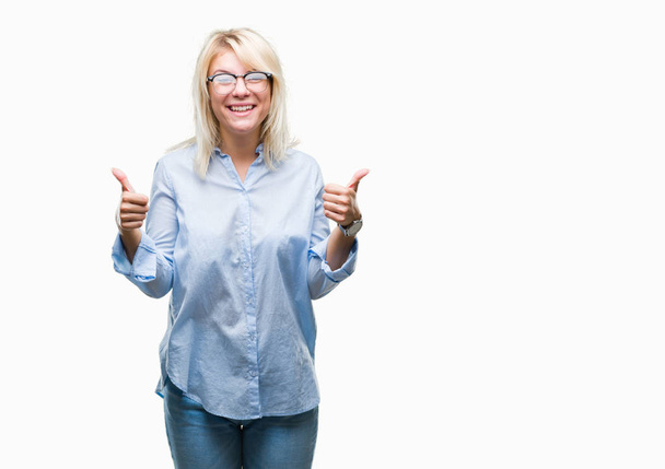 Young beautiful blonde business woman wearing glasses over isolated background success sign doing positive gesture with hand, thumbs up smiling and happy. Looking at the camera with cheerful expression, winner gesture. - Photo, Image
