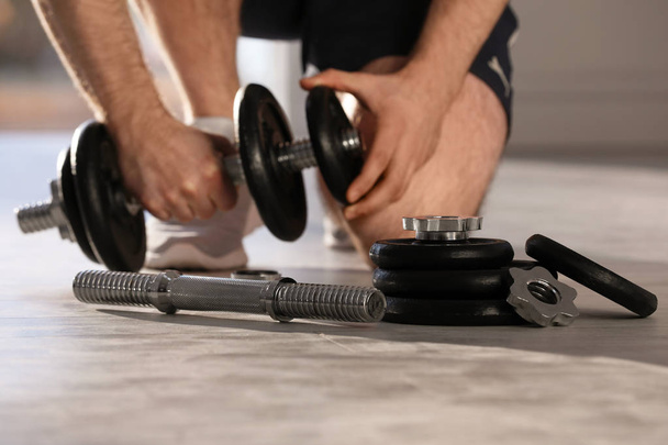 Male athlete with adjustable dumbbells indoors. Sports equipment - Photo, Image