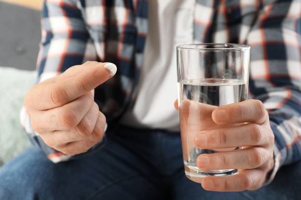 Man holding pill and glass of water indoors, closeup - 写真・画像
