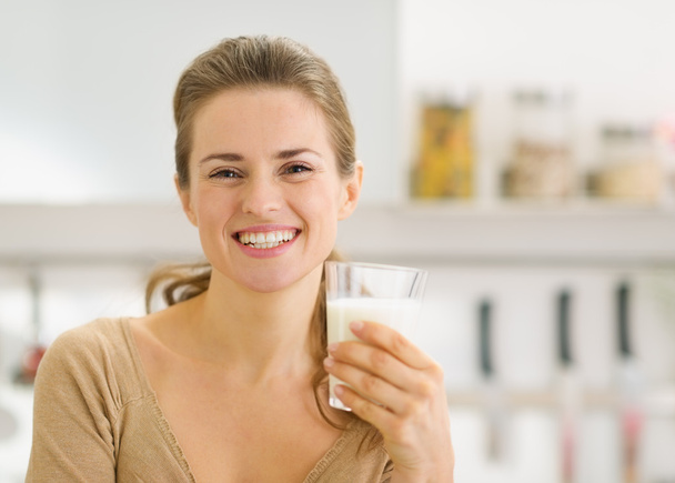Portrait of smiling young woman with glass of milk in kitchen - Фото, изображение