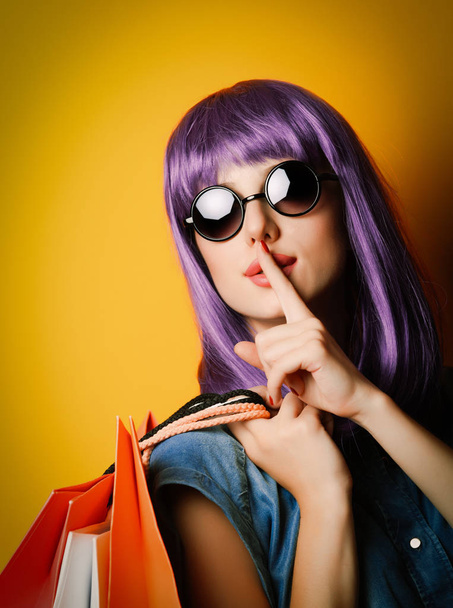 Woman with violet hair and sunglasses with shopping bags on yellow background - Foto, afbeelding