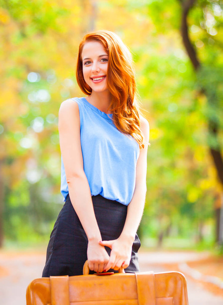 Happy redhead girl with suitcase in the autumn season time park. - Zdjęcie, obraz