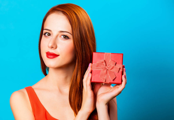 Smiling redhead woman with gift on blue background. - Photo, Image