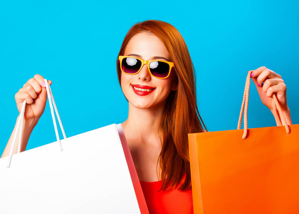 Style redhead woman holding shopping bags on blue background. - Foto, Imagem